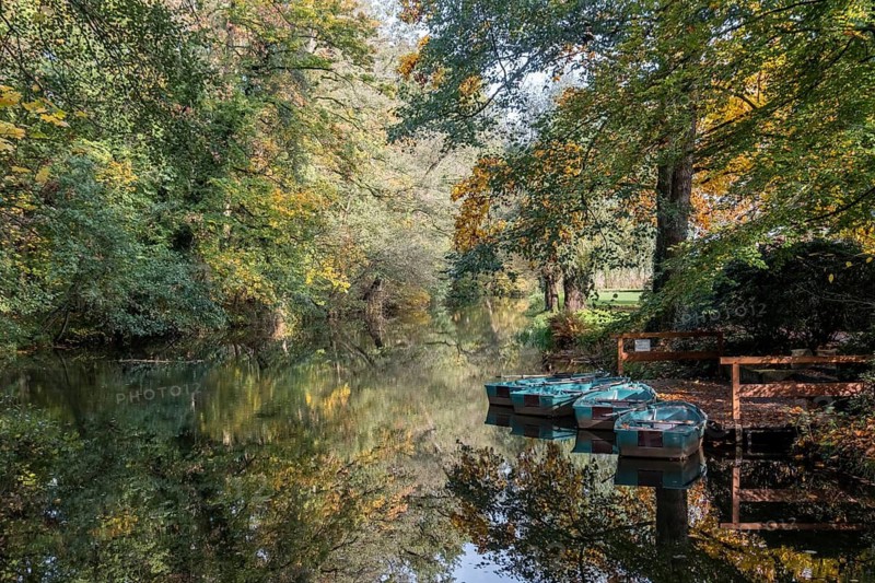 Quiet river with reflecting trees and resting boat in autumn, Ahaus-Alstätte, Münsterland, North Rhine-Westphalia, Germany