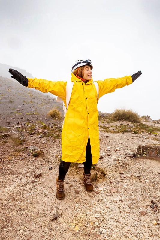 A hiker in a bright yellow raincoat embraces the rainy weather while trekking on a rugged mountain trail, showcasing the spirit of adventure and resilience in nature