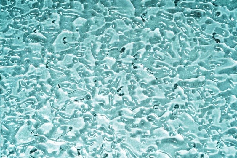 Top view of transparent gel smears covering a blue glass surface, creating a textured and abstract pattern. The image evokes a sense of fluidity and scientific exploration