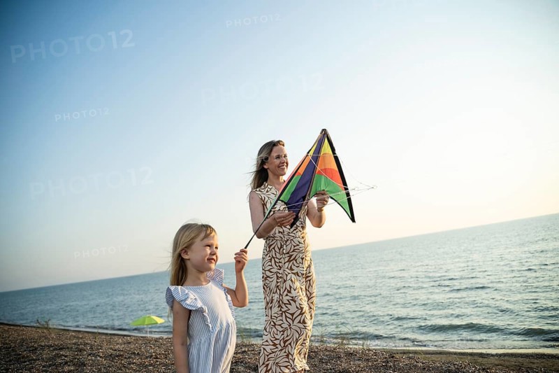A mother and daughter enjoy a special moment with a colorful kite on an Italian beach, sharing laughter and creating happy memories together