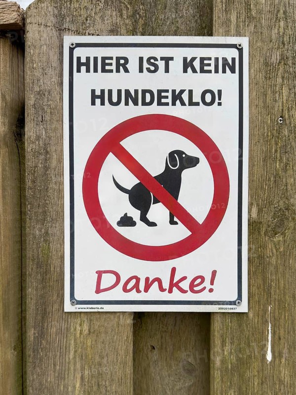 Sign with pictogram and inscription Hier ist kein Hundeklo on the outside of a wooden fence, Germany