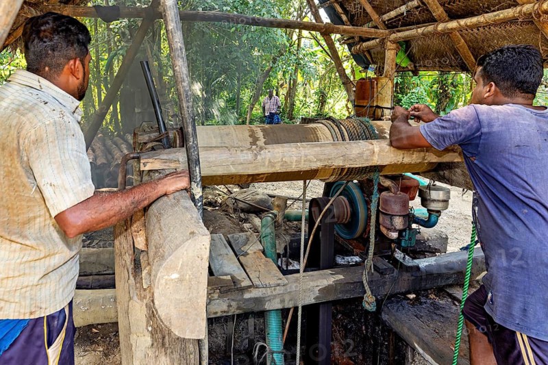 Two men stand by a wooden machine surrounded by outdoor nature, the sapphire and gemstone mines near Ratnapura in Sri Lanka