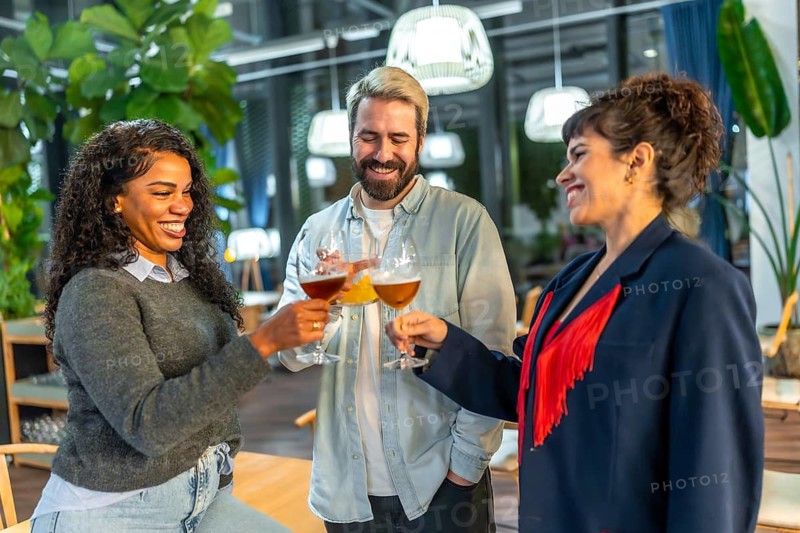 Multi-ethnic three happy friends toasting standing on a night bar terrace celebrating