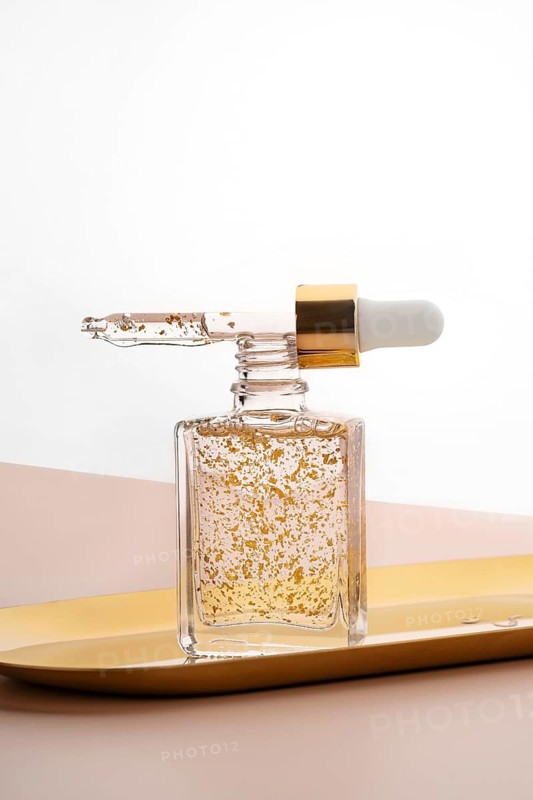 Luxurious anti-aging face serum showcased in a transparent glass bottle, enriched with visibly floating golden particles, ideal for enhancing skin radiance and youthful appearance