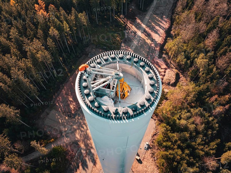A partially erected wind turbine protruding from a wooded area with technicians at work, Windrad Bau, Calmbach, Black Forest, Germany