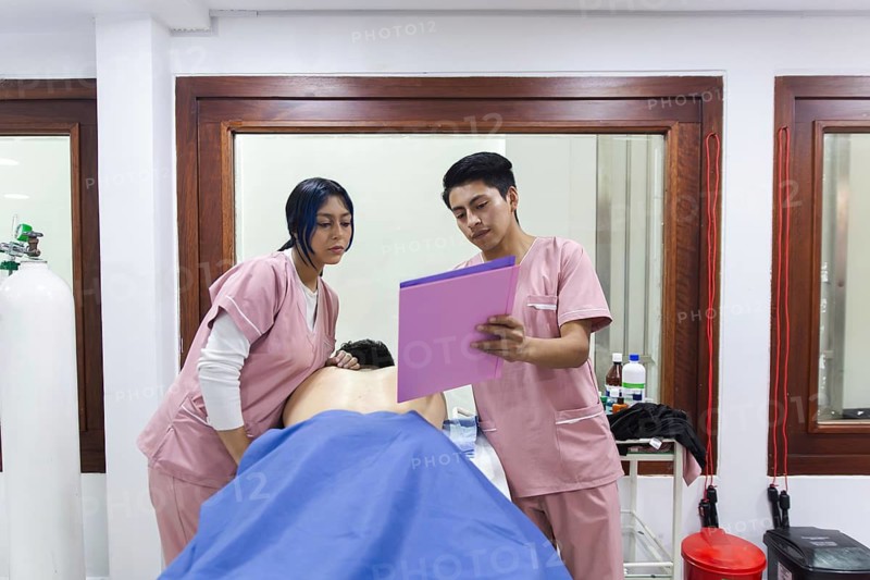 Physiotherapists work in a clinic in Ecuador, examining a patient's treatment plan. The setting highlights a professional and caring environment for rehabilitation