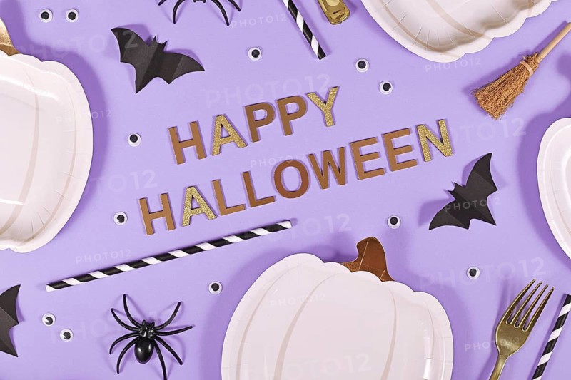 Happy Halloween text surrounded by pumpkin shaped plates, witch brooms, spiders and bats on purple background