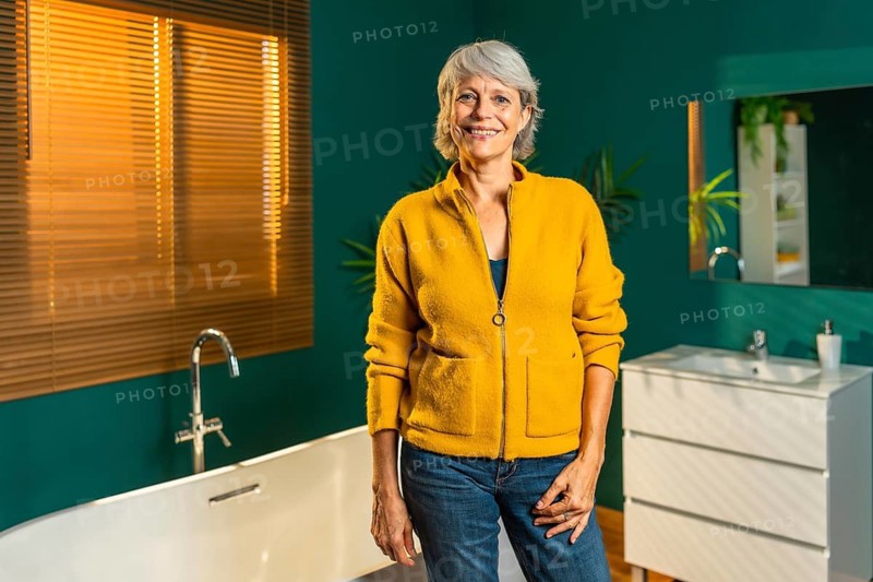 Three quarter length photo of a cheerful mature woman standing on the bathroom smiling at camera