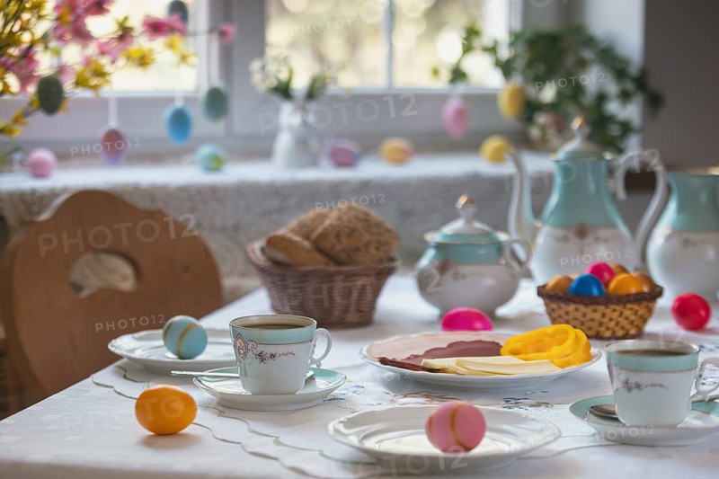 Breakfast table with Easter eggs, pastries and cold plate in front of decorated window