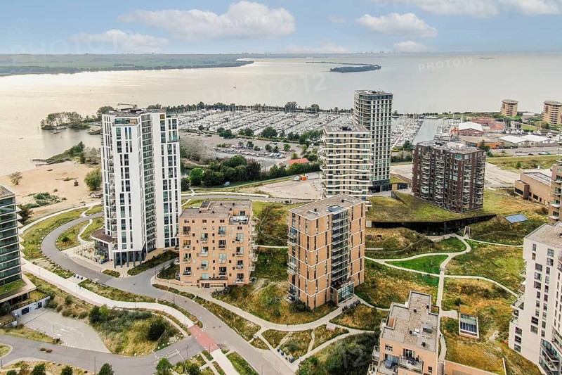 An expansive aerial view showcasing a blend of contemporary architecture, green spaces, and a bustling marina, highlighting urban development and nature coexisting harmoniously