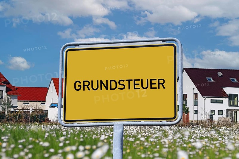Symbolic image of property tax: Town sign with the inscription GRUNDSTEUER in front of a new development area (Composing)