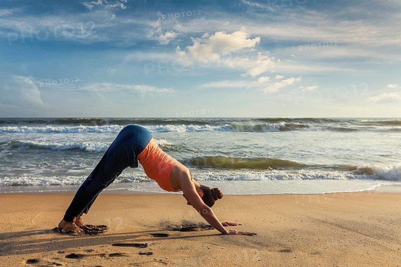 Yoga outdoors, young sporty fit woman doing Ashtanga Vinyasa yoga asana Adho mukha svanasana, downward facing dog, at tropical beach. Kerala, India