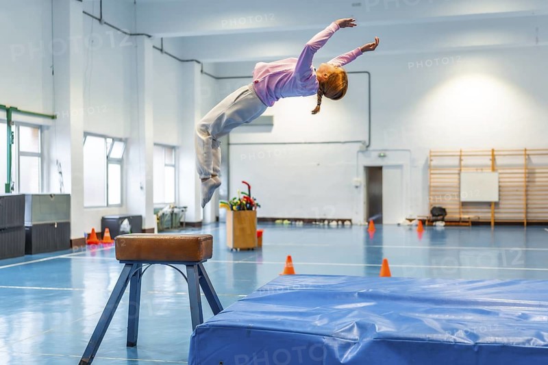Girl practicing gymnastics, jumping over a vaulting horse in a school gym, showcasing athleticism and dedication to the sport