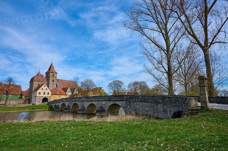 Stone bridge crosses river with view of an idyllic village with church and trees, spring, Ornbau, Triesdorf, Franconian Lake District, Ansbach District, Middle Franconia, Bavaria, Germany
