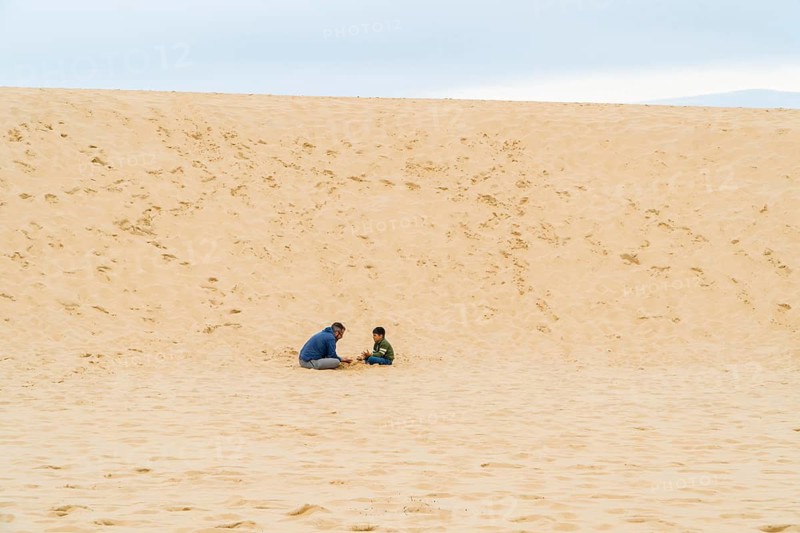 Father and child enjoy building sandcastles on an endless sandy desert under a cloudy sky. The empty expanse highlights their intimate bond and playful exploration in the dune of Pilat, France