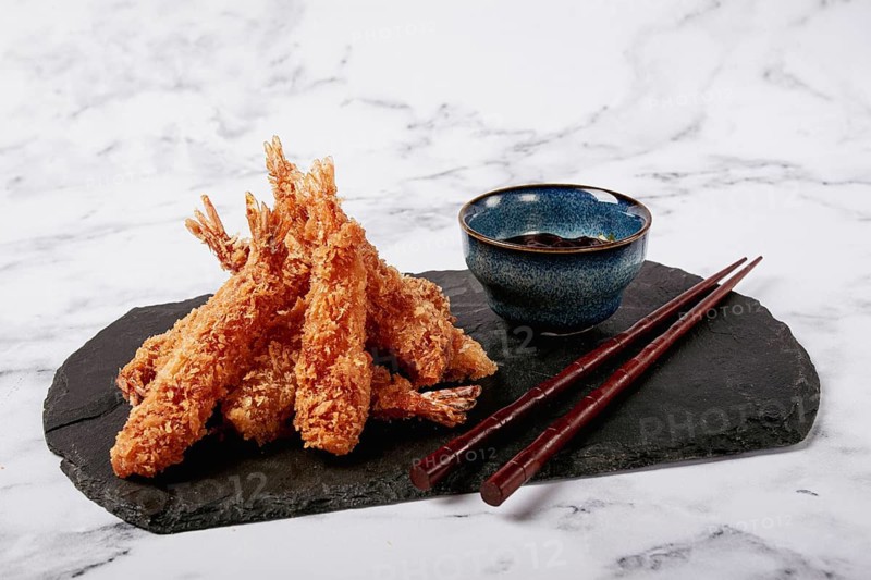 Shrimp in tempura, deep fried, on black slate, with sauce, light marble table, no people