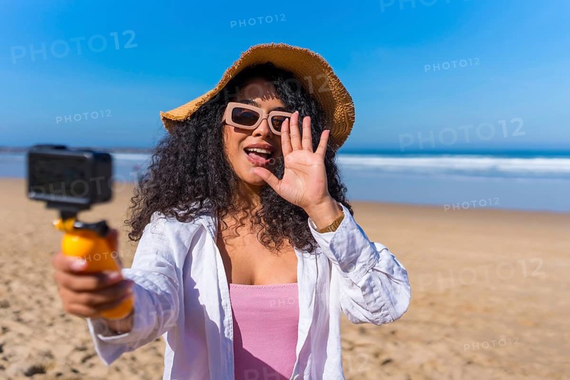 Young woman creating content for social media with an action camera on a sunny beach, sharing her vacation and travel experiences with online followers