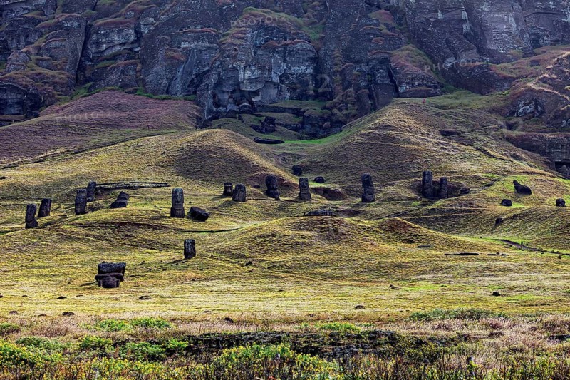 Several moai are spread over a gently rolling landscape under rocks, the moai statues on Easter Island in the Pacific Ocean
