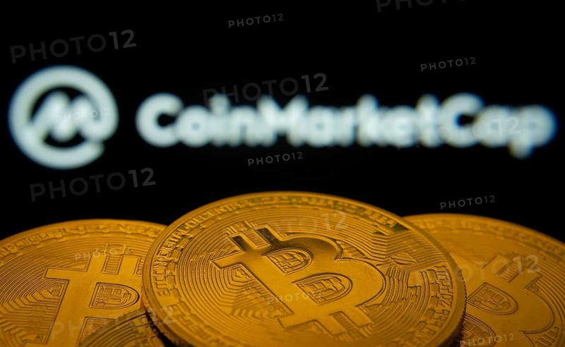 Dhaka, Bangladesh- 27 March 2025: Close-up of Bitcoin coins with the Coinmarketcap logo visible on a screen in the background
