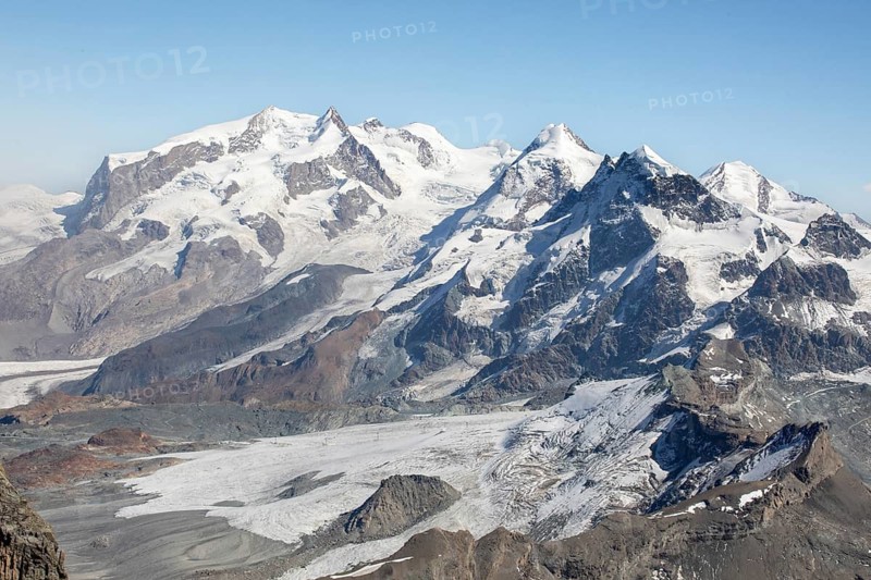 Majestic view of the snow-capped peaks of the Swiss Alps in Zermatt during summer. The rugged mountain terrain is contrasted by shimmering glaciers under a clear blue sky