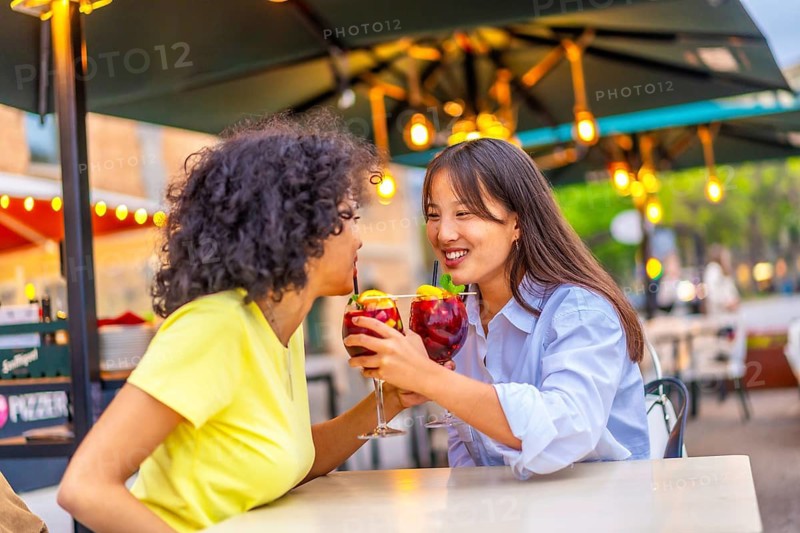 Romantic lesbian couple drinking cocktail together in an outdoor terrace enjoying summer in the city