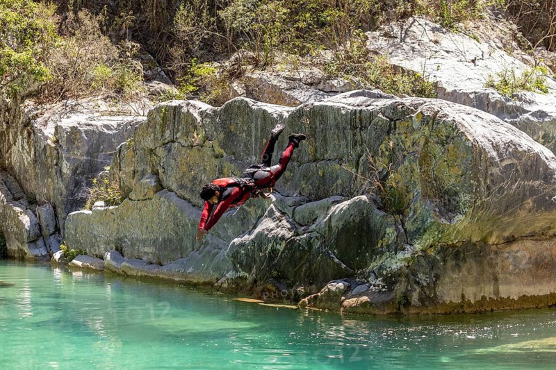 A canyoneer in full gear dives headfirst into a turquoise pool from a rocky ledge in Matacanes, Nuevo Leon, Mexico. The moment captures thrill, precision, and natural beauty
