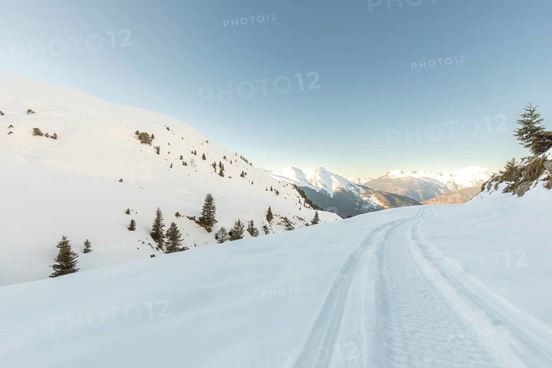 Snowmobile tracks carve a winding path through pristine snow-covered mountains, capturing the essence of winter adventure against a backdrop of clear blue skies and distant peaks