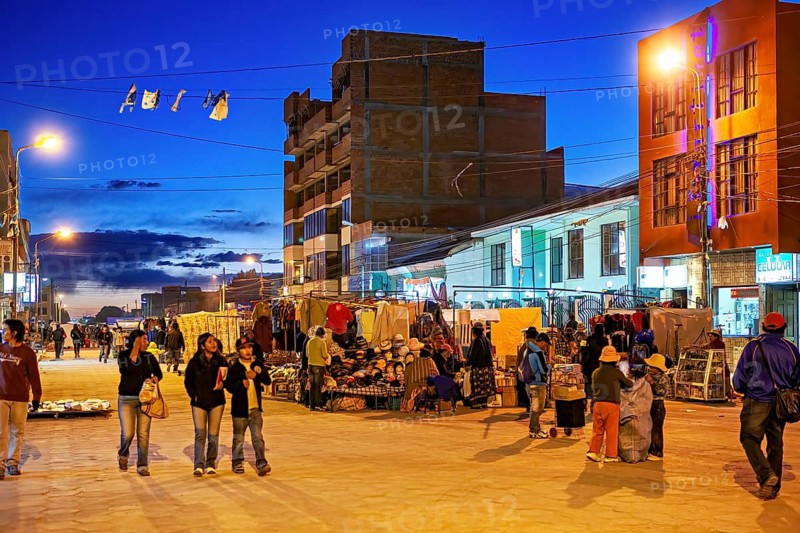 A busy marketplace at dusk with people, market stalls and illuminated buildings, The Uyuni Street Market in Bolivia