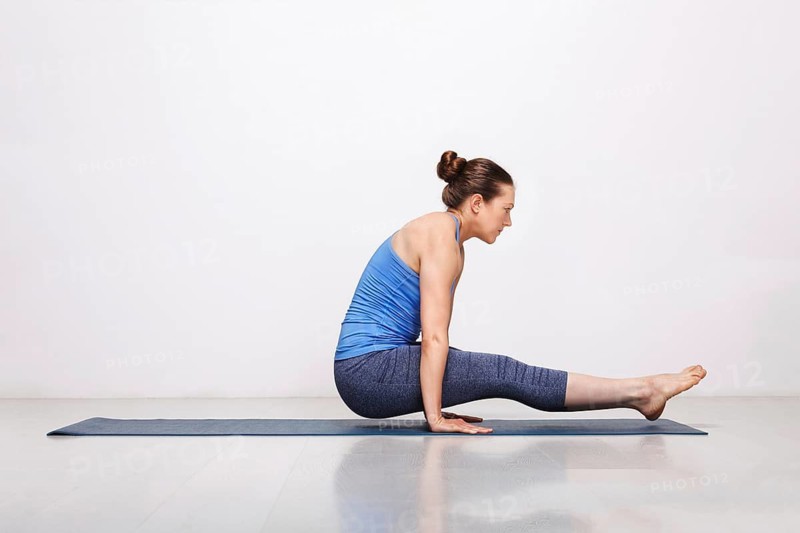 Woman doing Hatha asana Utpluti dandasana, lifted stuff pose on yoga mat on yoga mat in studio on grey bagckground