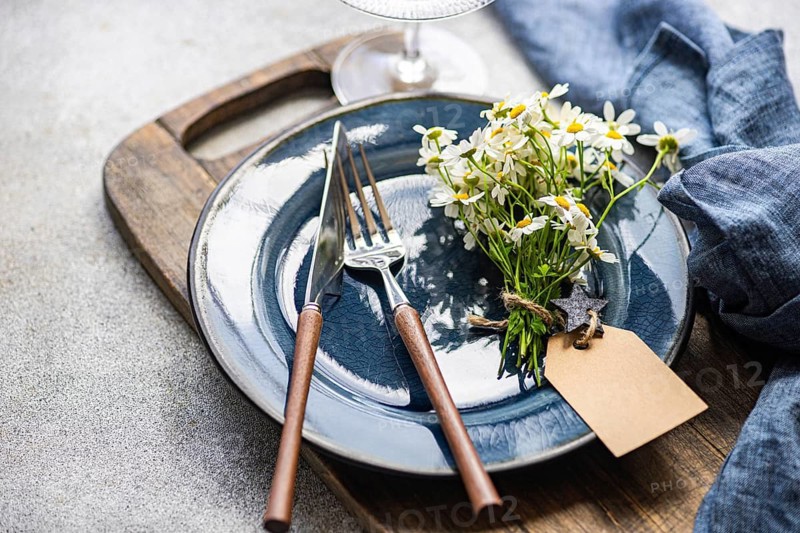 A charming arrangement of summer daisies rests elegantly on a blue ceramic plate with wooden cutlery on a rustic wooden board. Aesthetic and cozy interior decor