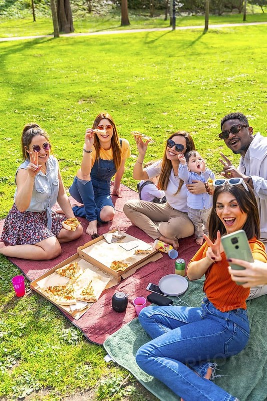 Friends are having a picnic in a park, eating pizza, taking selfies and enjoying time together
