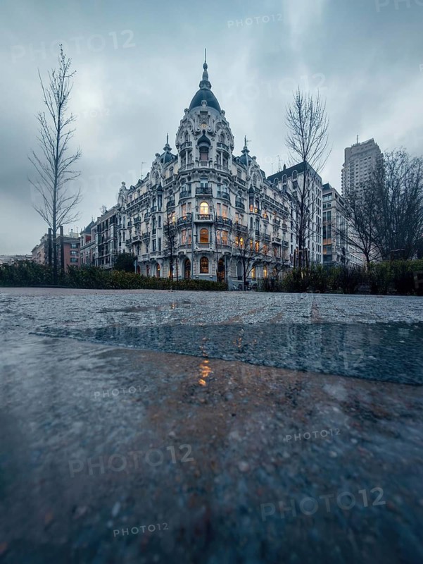 Elegant historic building of Madrid with ornate facade and soft warm lighting at dusk. A tranquil, cloudy urban scene with reflections on wet pavement, enhancing the serene atmosphere