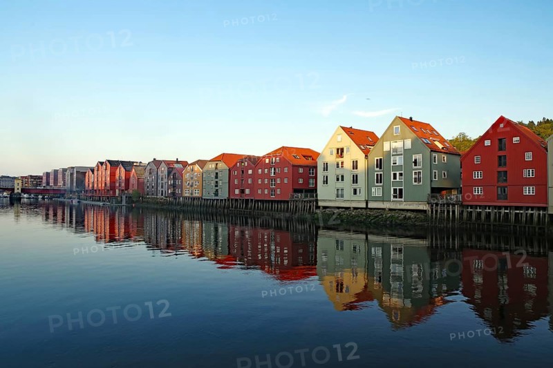 Row of colourful houses on the waterfront with clear reflection on the water surface under a clear sky, Nideleva, Trondheim, Tröndelag, Norway