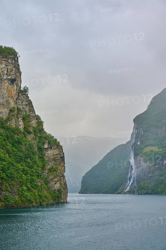 Geiranger Fjord with waterfall surrounded by rocks and mountains with overcast sky, Geiranger, Geiranger Fjord, Stranda, Romsdal, Norway