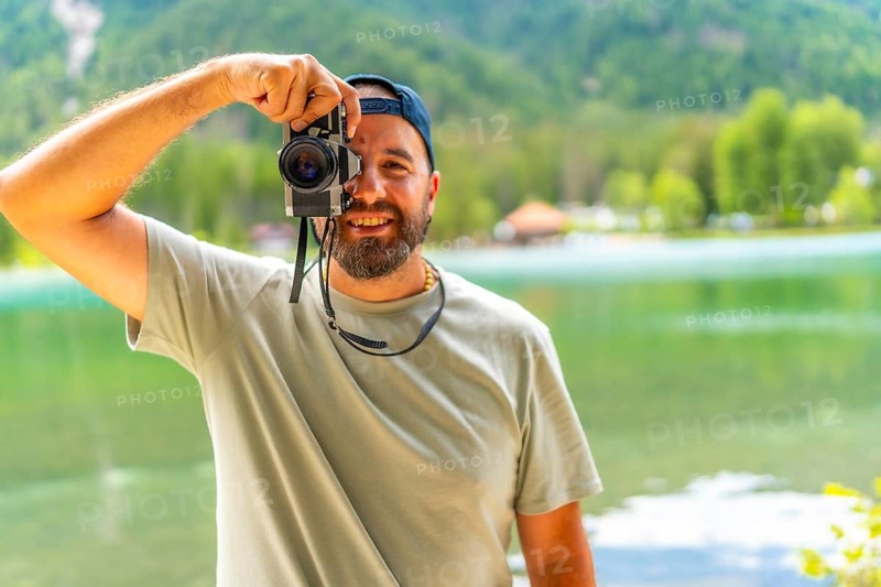 Smiling tourist taking pictures with a vintage camera at lake dobbiaco, a popular destination in the italian dolomites during summer holidays