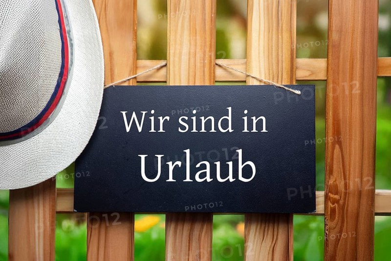 Company holidays Symbolic image: Sign with added text WIR SIND IN URLAUB on a wooden fence