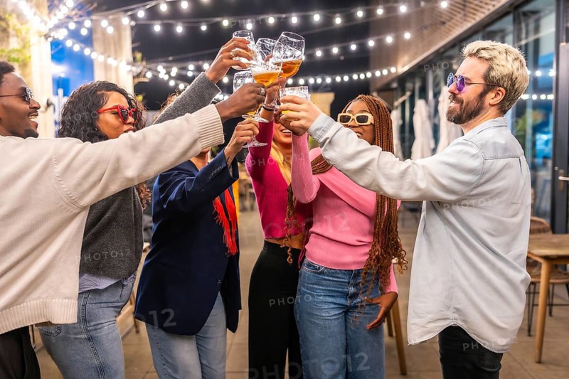 Multi-ethnic group of friends toasting in a bar terrace at night
