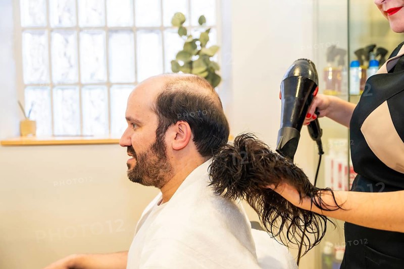 Hairdresser drying a washed capillary prosthesis before attaching it to the head of a man