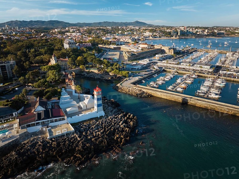 Aerial view of Santa Marta lighthouse and Cascais marina with moored yacht boats with Cascais cityscape, Portugal on sunset