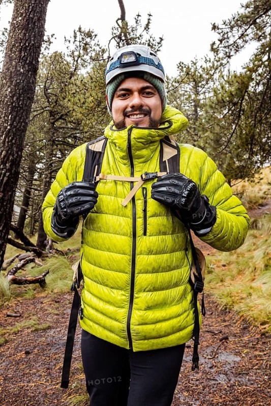 A hiker wearing bright green gear navigates a muddy, rain-soaked trail through a dense forest. Equipped for adventure, the hiker embraces the challenges of the wet terrain