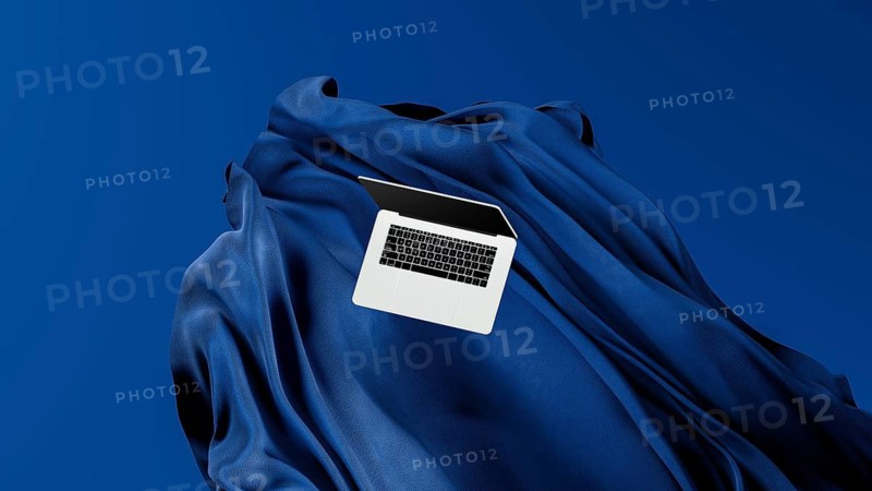A sleek laptop is placed atop smooth fabric, showcasing its lightweight design against a rich blue backdrop