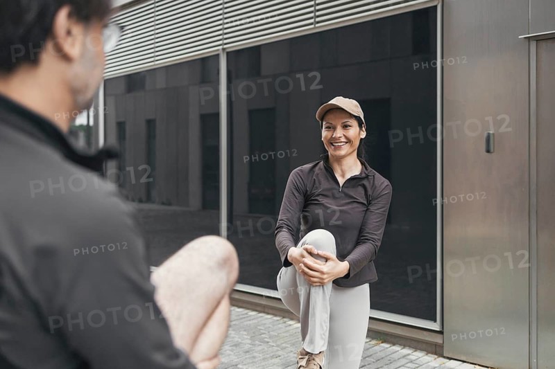 A couple enjoys stretching outdoors, preparing for a sports activity. Both are dressed in athletic wear, demonstrating teamwork and motivation for a healthy, active lifestyle