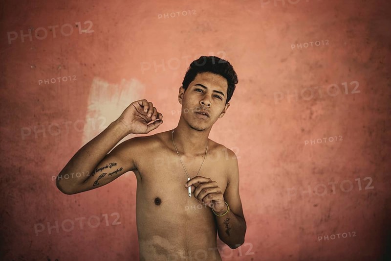 A boy smokes a cigarrette at the grave of the social bandit Malandro Ismael, Cementerio General del Sur, Caracas, Venezuela