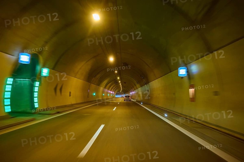 Illuminated motorway tunnel with several lights and signs, Switzerland