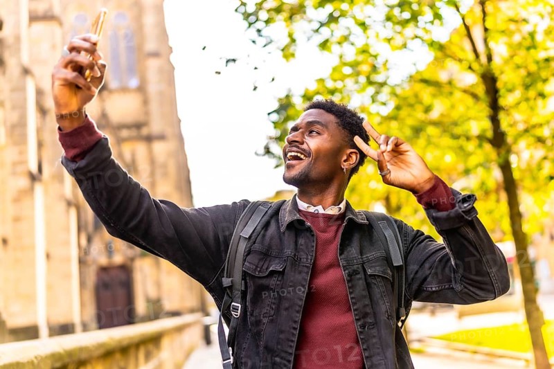 Cool african man taking selfie gesturing success walking at street exploring a city under the sunset