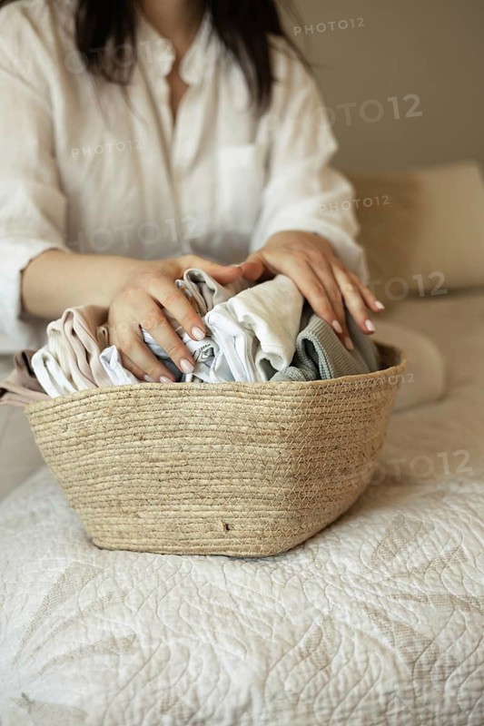A pregnant woman gently folds baby clothes in a woven basket, preparing for the arrival of her baby. Her delicate actions reflect anticipation and excitement for motherhood