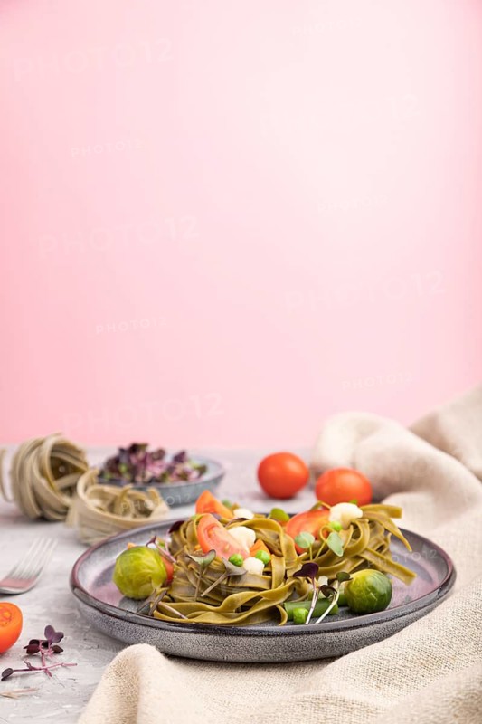Tagliatelle green spinach pasta with tomato, pea and microgreen sprouts on a gray and pink background and linen textile. Side view, copy space, selective focus
