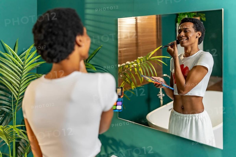 Reflection on the mirror of a latin happy gay man making up in the bathroom