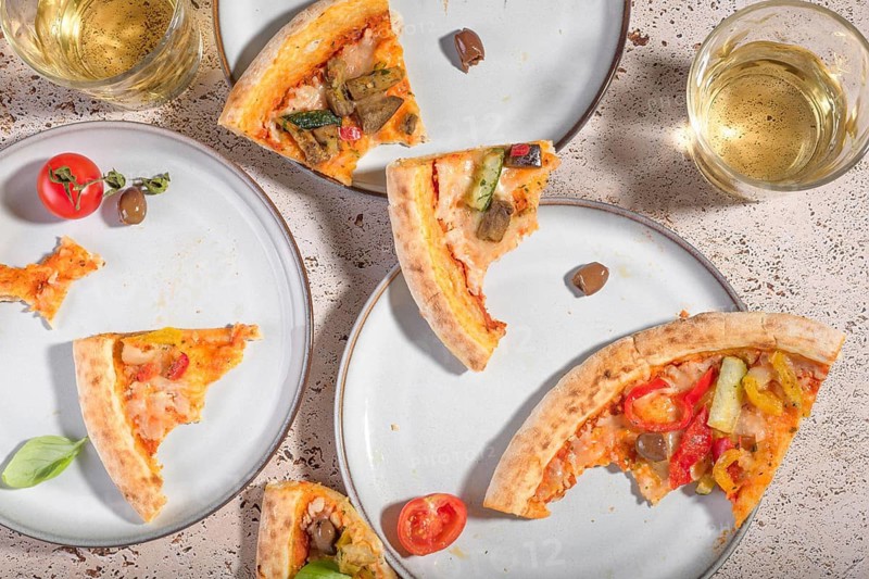 Fresh vegetarian pizza slices topped with zucchini, eggplant, peppers, olives, and tomatoes, served on a rustic table. A delicious plant-based meal ideal for lunch