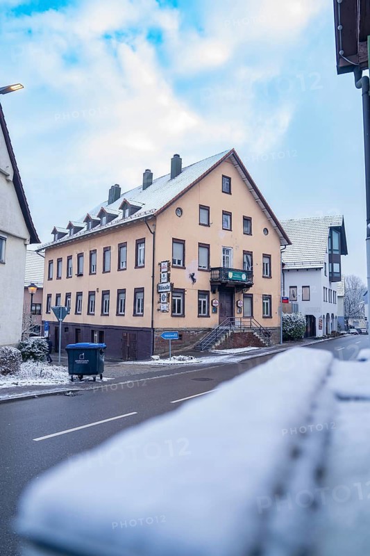 Large inn on a snow-covered road under a partly cloudy sky, Aidlingen, Böblingen district, Germany
